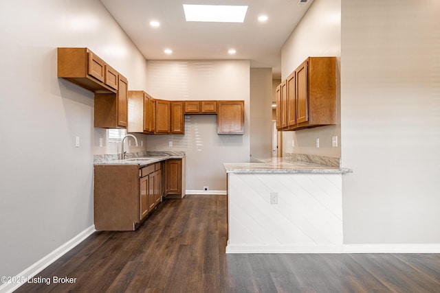 kitchen with dark wood-style floors, a peninsula, a skylight, brown cabinetry, and a sink