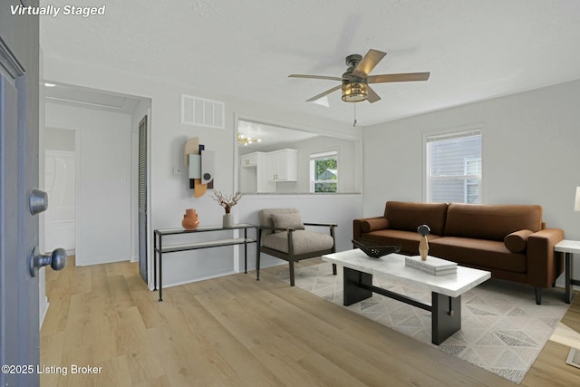 living room featuring light wood-type flooring, visible vents, a textured ceiling, and a ceiling fan