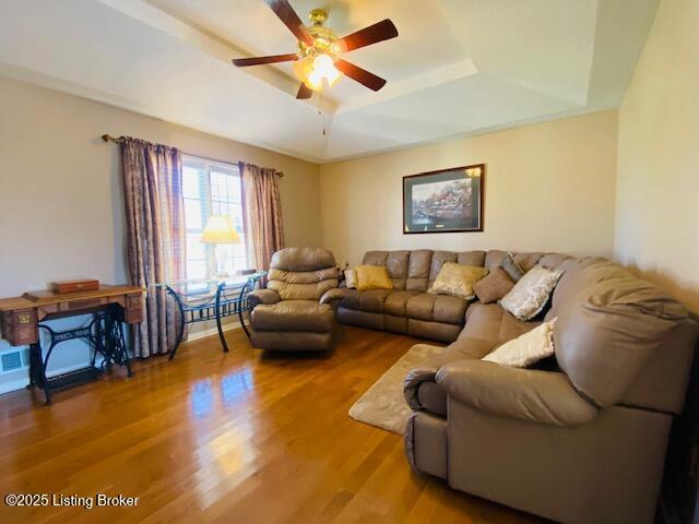 living area featuring ceiling fan, a tray ceiling, and wood finished floors