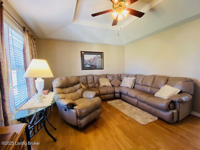 living area with ceiling fan, a raised ceiling, and wood finished floors