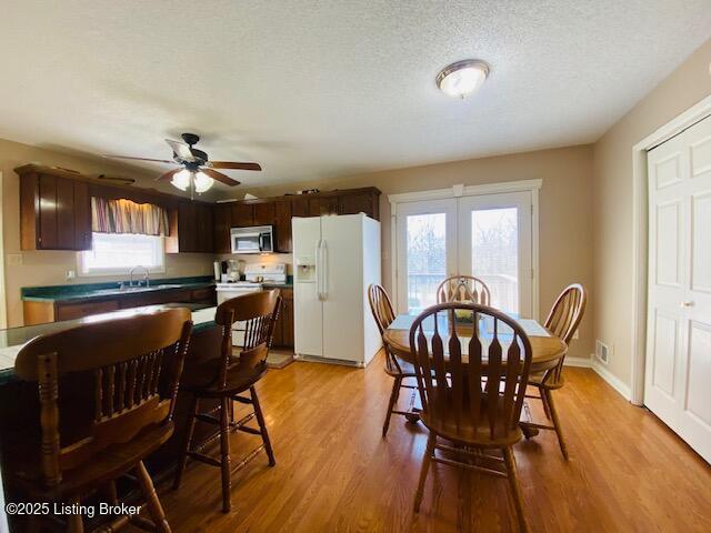 dining room with visible vents, baseboards, light wood-style floors, a textured ceiling, and a ceiling fan