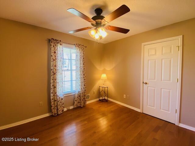 empty room featuring wood finished floors, baseboards, and ceiling fan