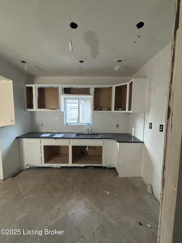 kitchen with dark countertops, a sink, white cabinets, and open shelves