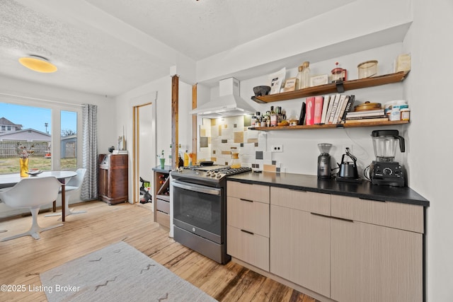 kitchen with stainless steel gas range, custom exhaust hood, light wood-style flooring, open shelves, and dark countertops