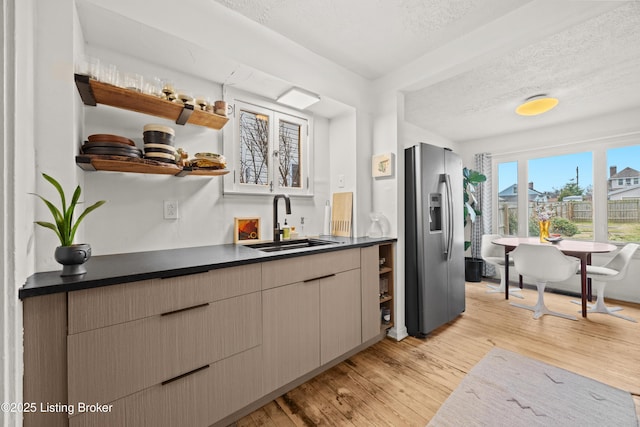 kitchen with dark countertops, a sink, light wood-style flooring, and stainless steel fridge with ice dispenser