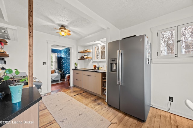 kitchen featuring light wood finished floors, a sink, stainless steel refrigerator with ice dispenser, plenty of natural light, and open shelves