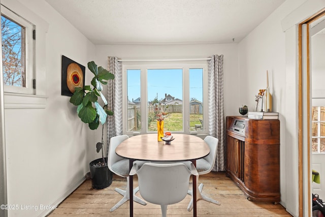 dining area with light wood-type flooring, baseboards, and a textured ceiling