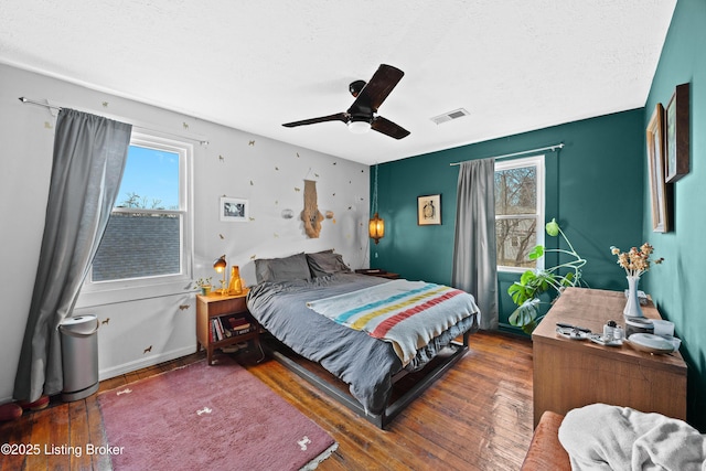 bedroom with ceiling fan, visible vents, multiple windows, and wood-type flooring