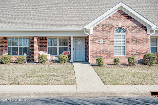 exterior space with brick siding, a shingled roof, and a front lawn