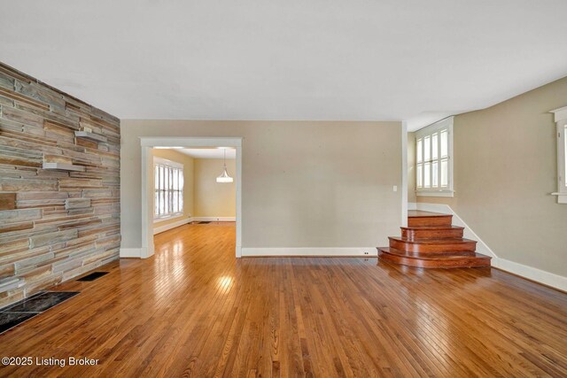 unfurnished living room with visible vents, plenty of natural light, baseboards, and hardwood / wood-style flooring