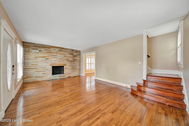 unfurnished living room featuring a stone fireplace, a healthy amount of sunlight, stairway, and light wood-style flooring