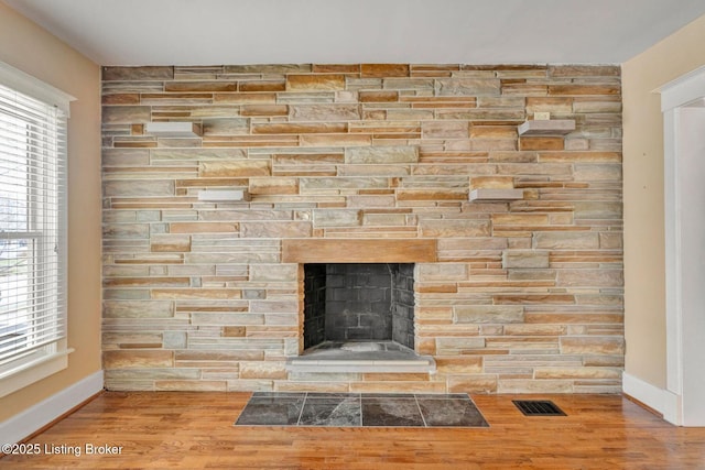 details with a stone fireplace, wood finished floors, visible vents, and baseboards