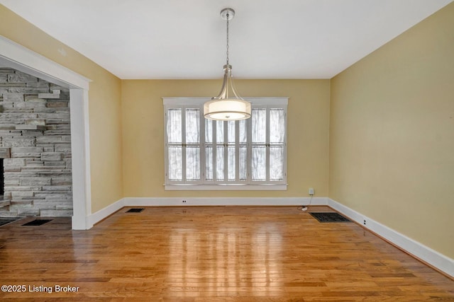 unfurnished dining area featuring a stone fireplace, wood finished floors, visible vents, and baseboards