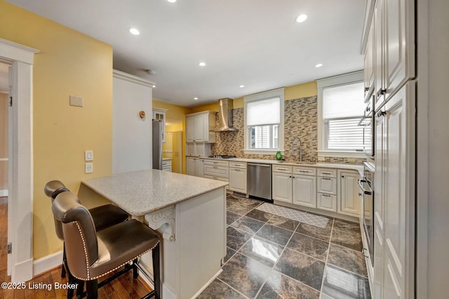 kitchen featuring a breakfast bar, stainless steel appliances, a peninsula, wall chimney range hood, and decorative backsplash