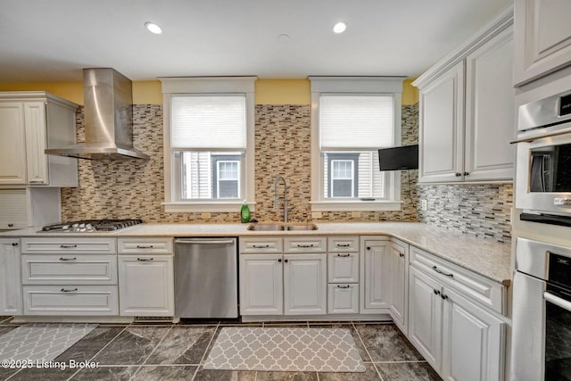 kitchen with a sink, stainless steel appliances, decorative backsplash, and wall chimney range hood