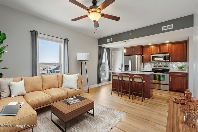 living area featuring light wood-type flooring, visible vents, baseboards, and ceiling fan