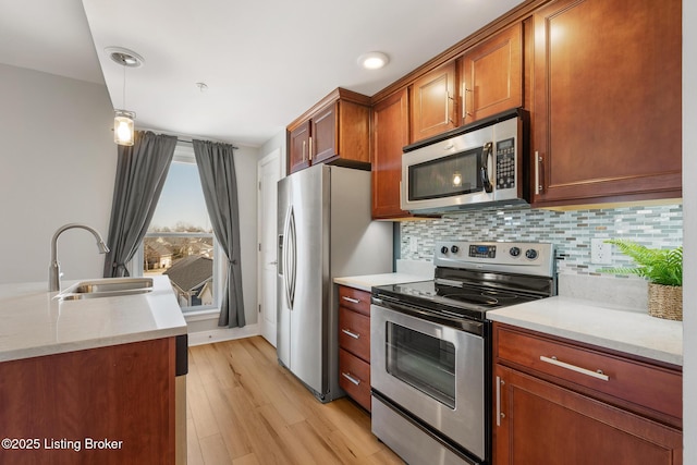 kitchen with a sink, tasteful backsplash, stainless steel appliances, light wood finished floors, and hanging light fixtures