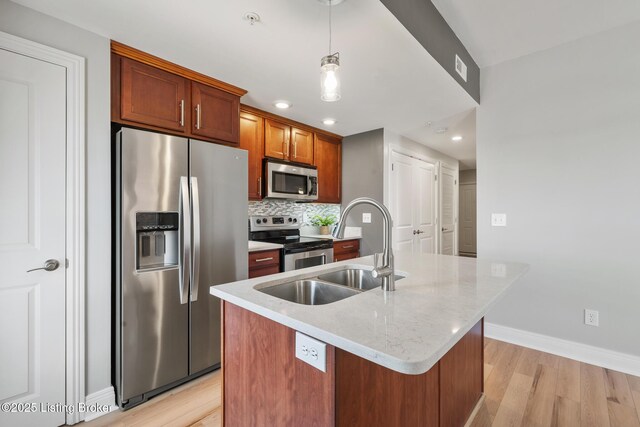 kitchen featuring tasteful backsplash, light wood-style flooring, appliances with stainless steel finishes, hanging light fixtures, and a kitchen island with sink