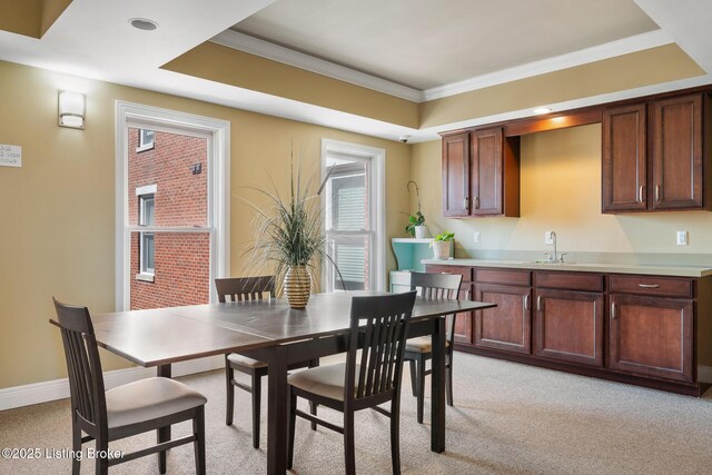 dining room with baseboards, light colored carpet, a raised ceiling, and ornamental molding