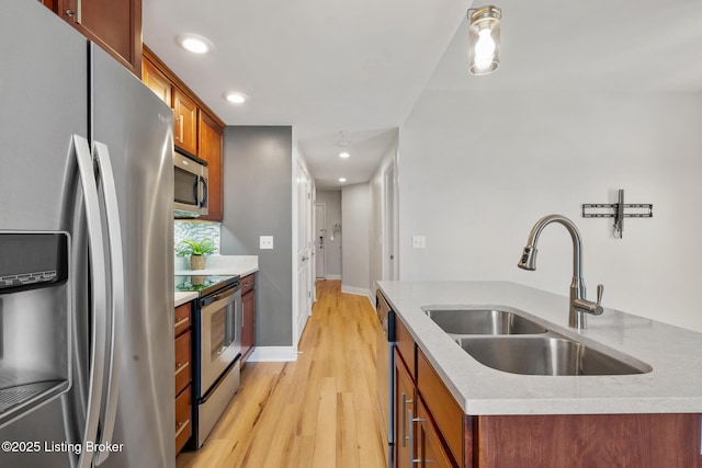 kitchen with a center island with sink, light wood finished floors, a sink, appliances with stainless steel finishes, and brown cabinets