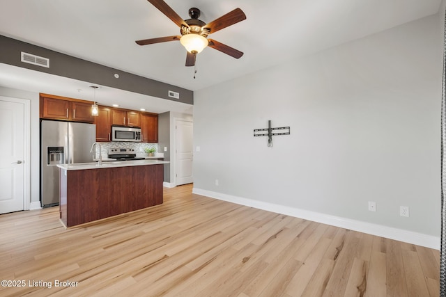 kitchen featuring light wood-style flooring, a kitchen island with sink, stainless steel appliances, decorative backsplash, and light countertops