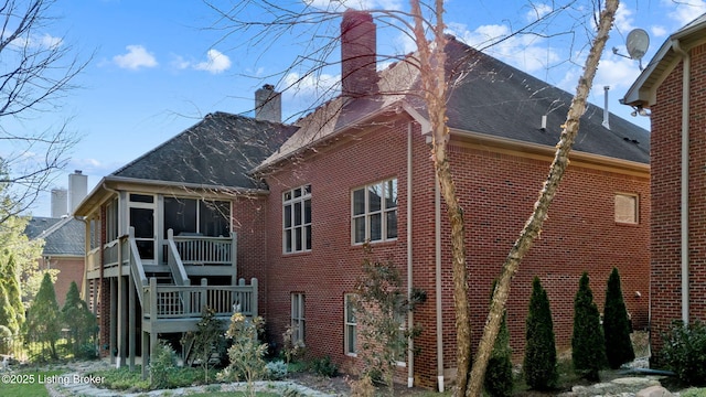 rear view of property featuring a sunroom, a shingled roof, stairs, a chimney, and brick siding