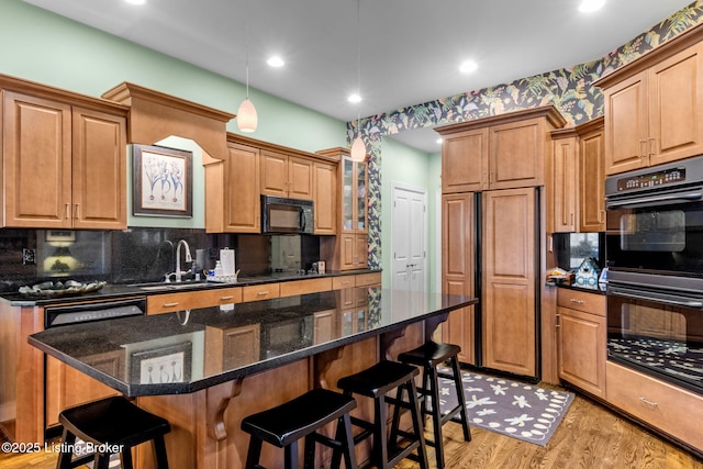 kitchen featuring light wood finished floors, a breakfast bar area, decorative backsplash, black appliances, and a sink