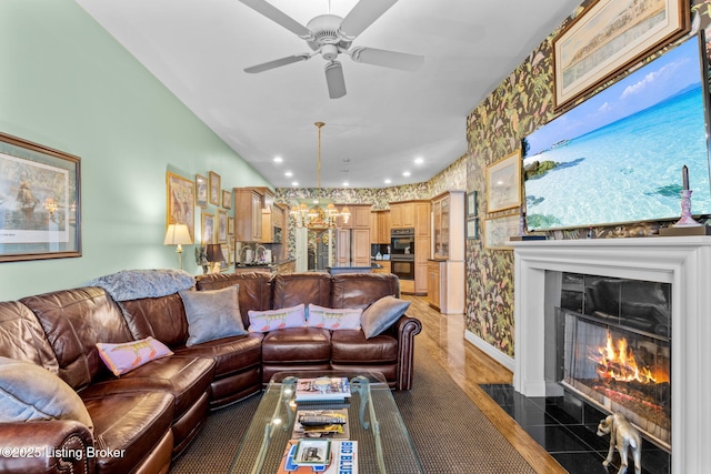 living area with wallpapered walls, a fireplace with flush hearth, lofted ceiling, recessed lighting, and ceiling fan with notable chandelier