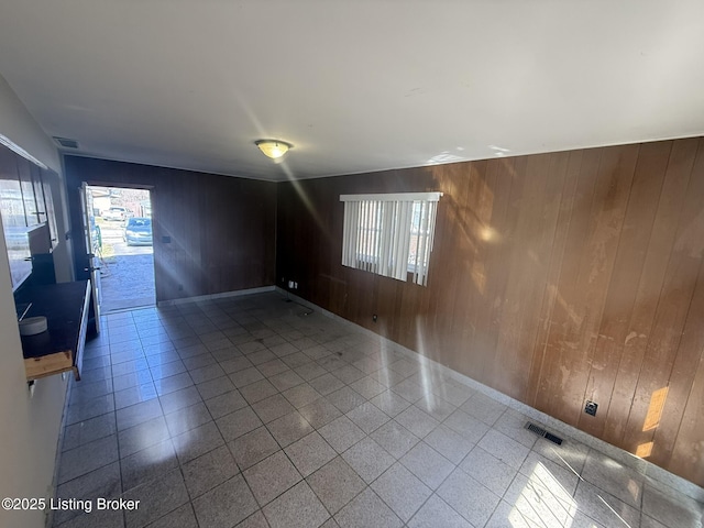 unfurnished room with visible vents, wood walls, and tile patterned floors