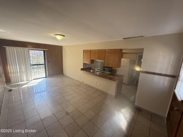 kitchen with visible vents, dark countertops, freestanding refrigerator, a peninsula, and a sink