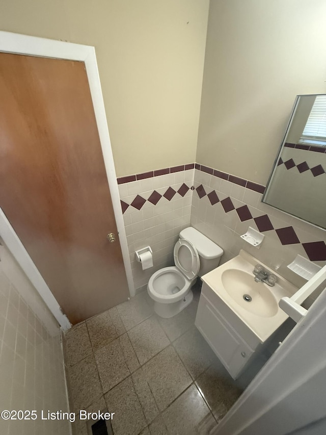 bathroom featuring toilet, vanity, tile walls, and wainscoting