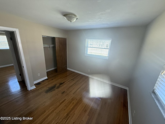 unfurnished bedroom featuring dark wood-type flooring, a closet, and baseboards