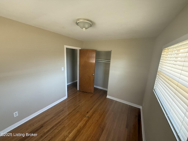 unfurnished bedroom featuring dark wood-style floors, a closet, and baseboards