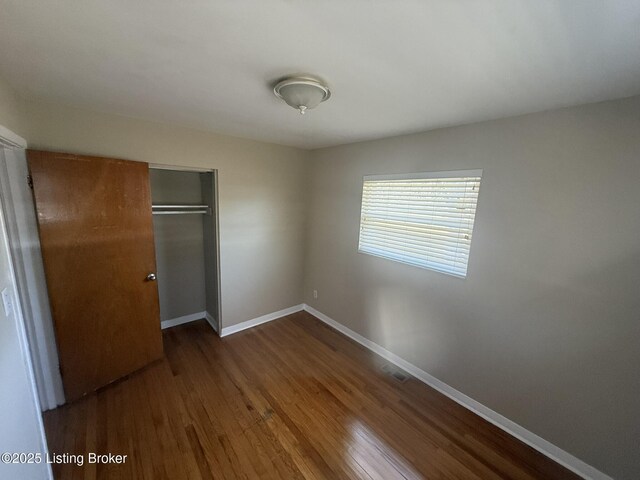 unfurnished bedroom featuring a closet, wood finished floors, visible vents, and baseboards