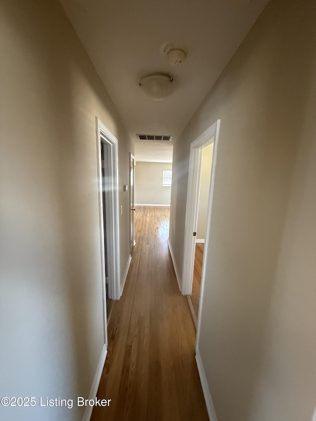 hallway with wood finished floors, visible vents, and baseboards