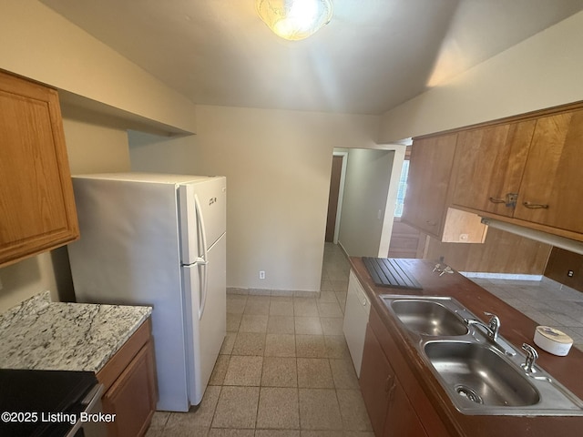 kitchen with baseboards, brown cabinets, a sink, and freestanding refrigerator