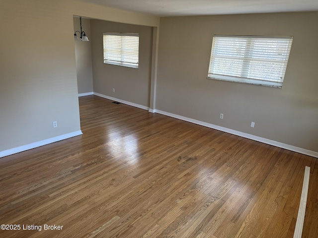 unfurnished room featuring a chandelier, baseboards, and wood finished floors