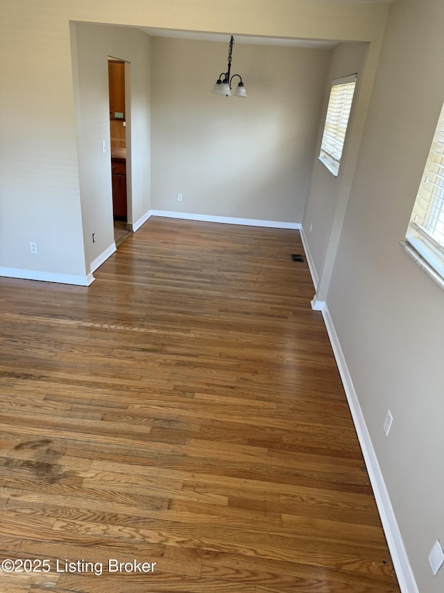 unfurnished dining area with a notable chandelier, wood finished floors, visible vents, and baseboards