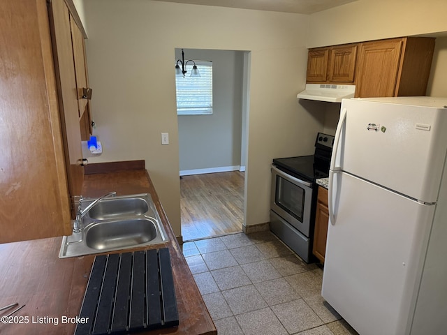 kitchen with brown cabinets, stainless steel electric range oven, freestanding refrigerator, a sink, and exhaust hood