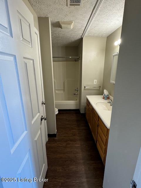 full bath with visible vents, vanity, wood finished floors, a textured ceiling, and washtub / shower combination