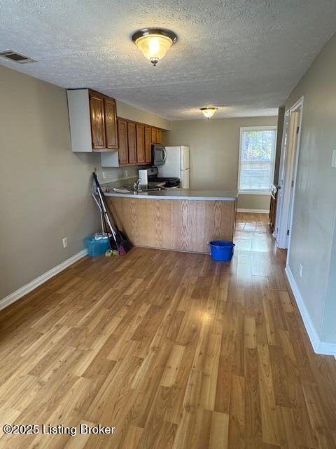 kitchen with visible vents, brown cabinets, a peninsula, and light wood finished floors