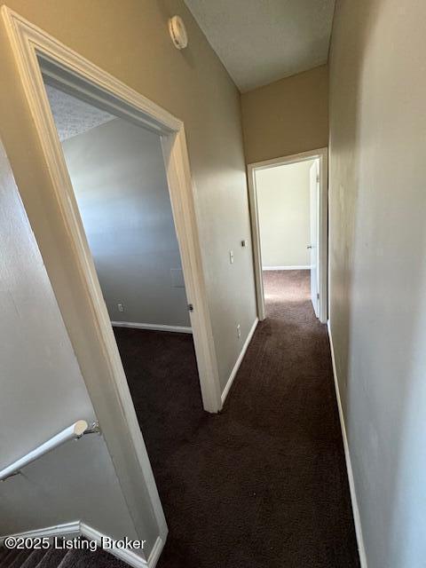 hall with baseboards and dark colored carpet