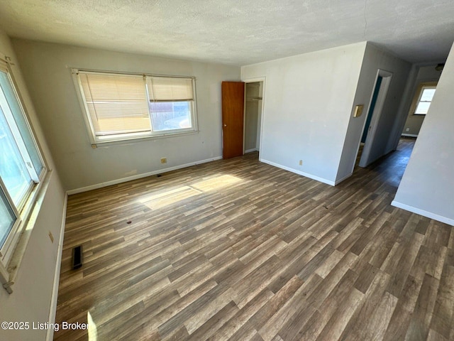 empty room with a textured ceiling, dark wood-style flooring, visible vents, baseboards, and a wealth of natural light