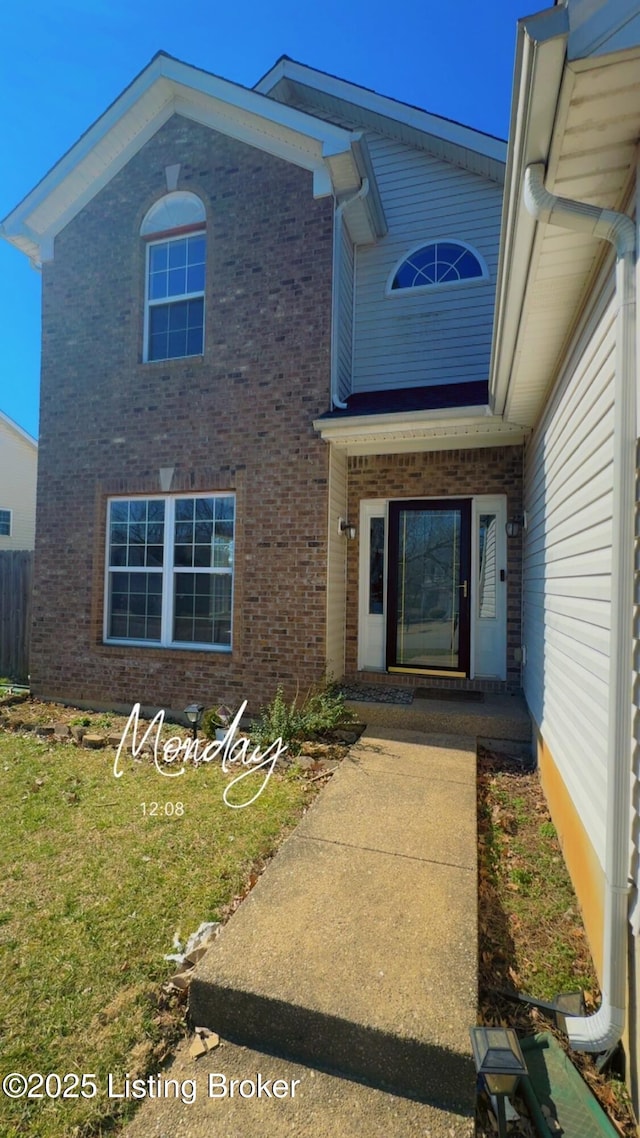 view of exterior entry with a lawn and brick siding