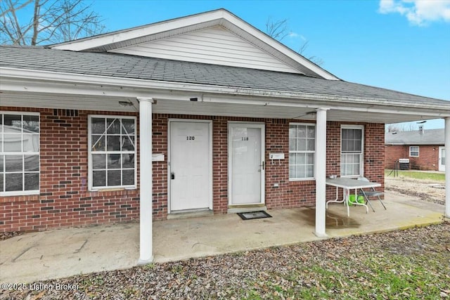 exterior space with covered porch, brick siding, and roof with shingles