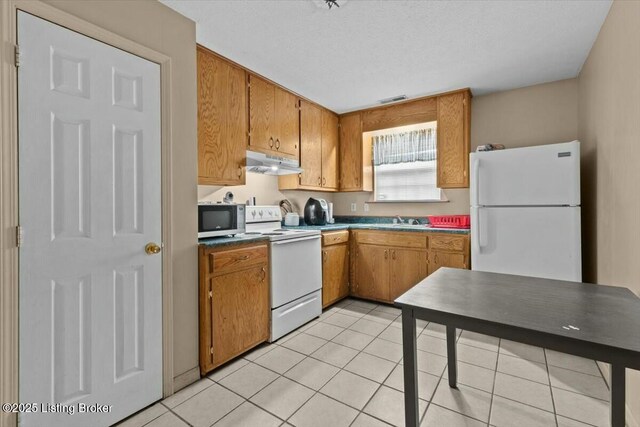 kitchen with white appliances, under cabinet range hood, brown cabinets, and a sink