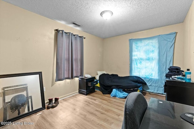 bedroom with a textured ceiling, wood finished floors, visible vents, and baseboards