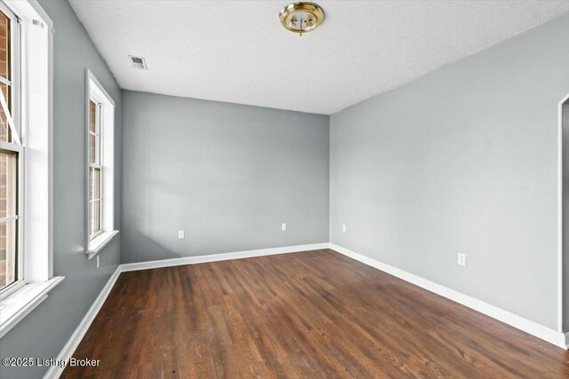 empty room with wood finished floors, visible vents, and baseboards