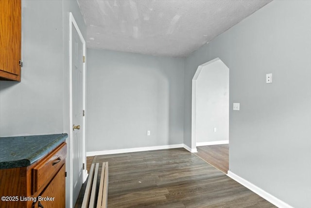 interior space with dark wood-style floors, brown cabinetry, arched walkways, and baseboards