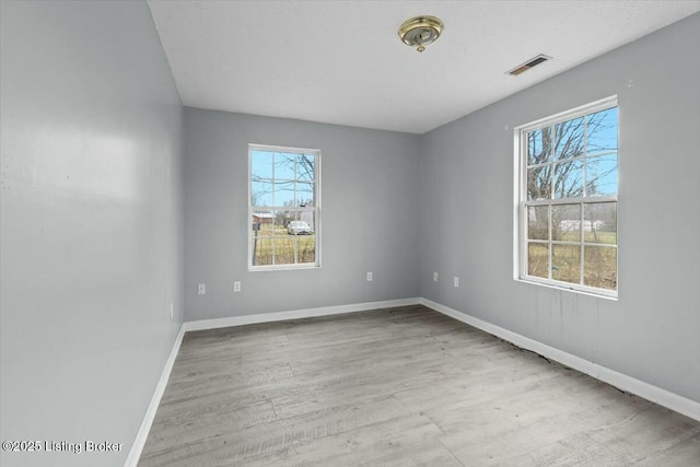 unfurnished room with baseboards, wood finished floors, visible vents, and a healthy amount of sunlight